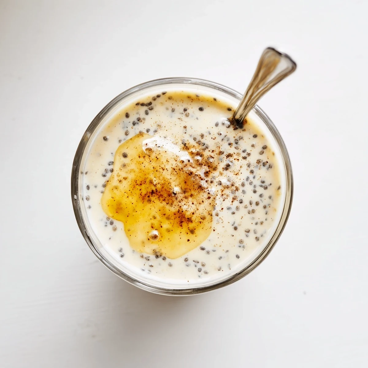 Glass of refreshing Greek yogurt banana smoothie topped with cinnamon and chia seeds on a wooden counter