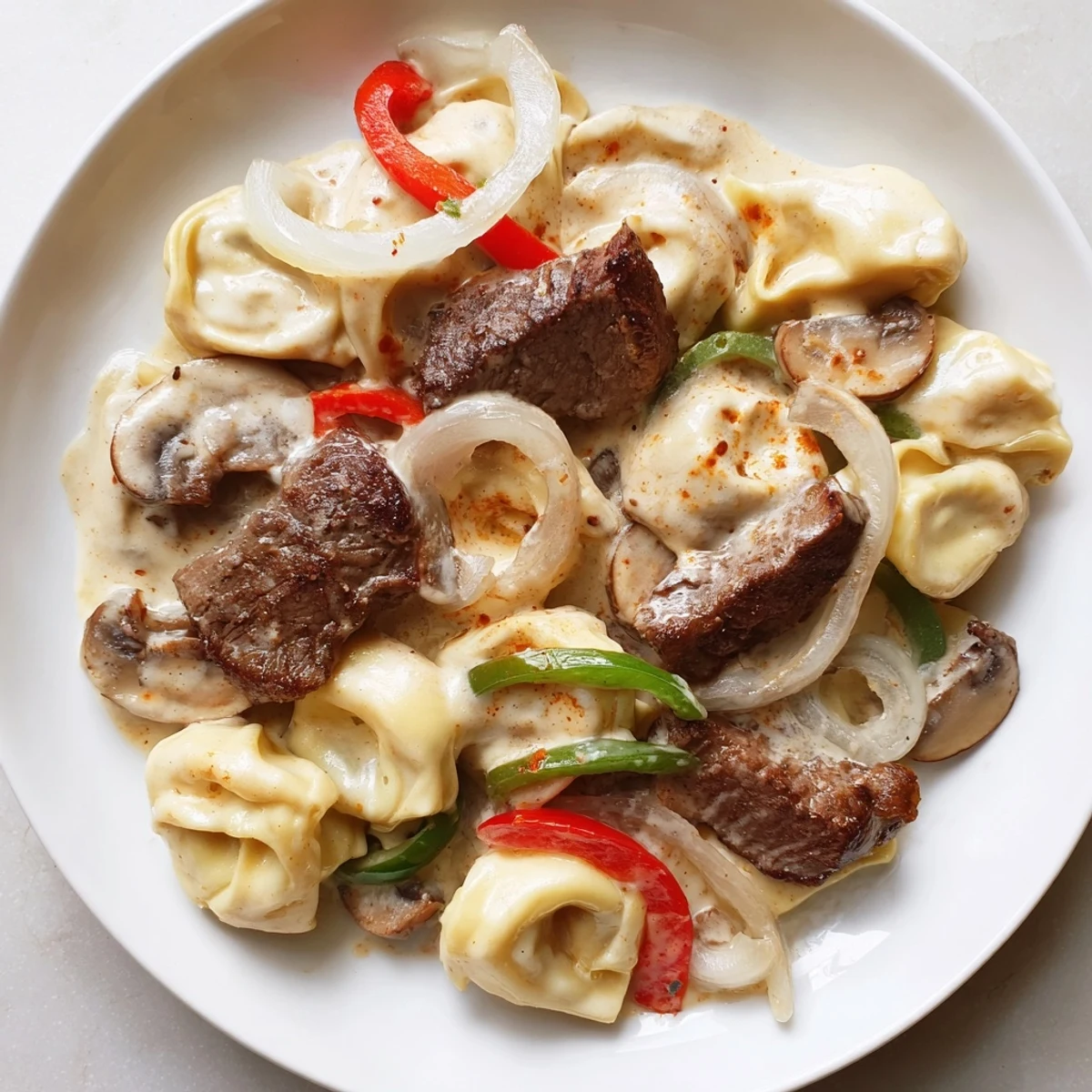 Slow cooker Crock Pot Cheesesteak Tortellini featuring tender beef, melted provolone, and colorful bell peppers in creamy sauce.