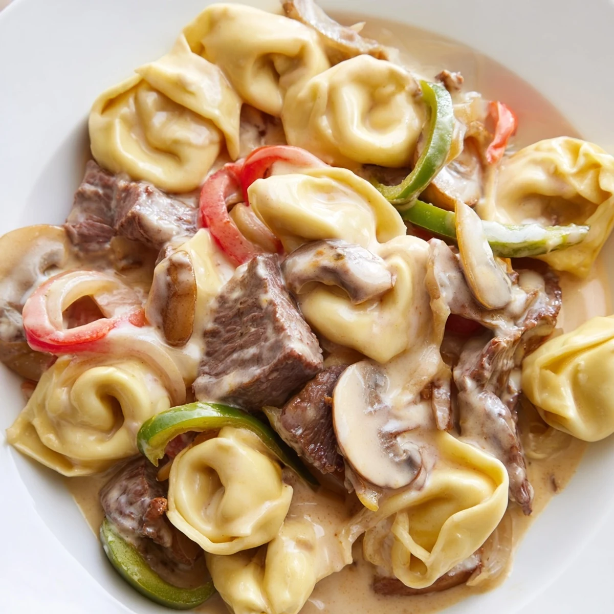 Hearty Crock Pot Cheesesteak Tortellini served hot with golden melted mozzarella, seared beef strips, and vibrant red and green peppers.