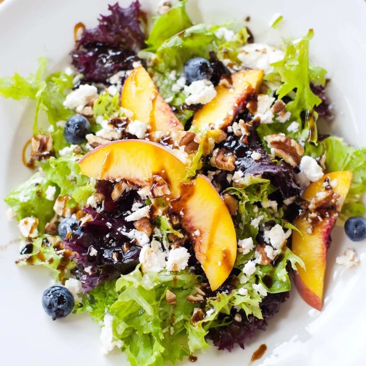 Colorful blueberry peach feta salad topped with toasted pecans on white dinner plate