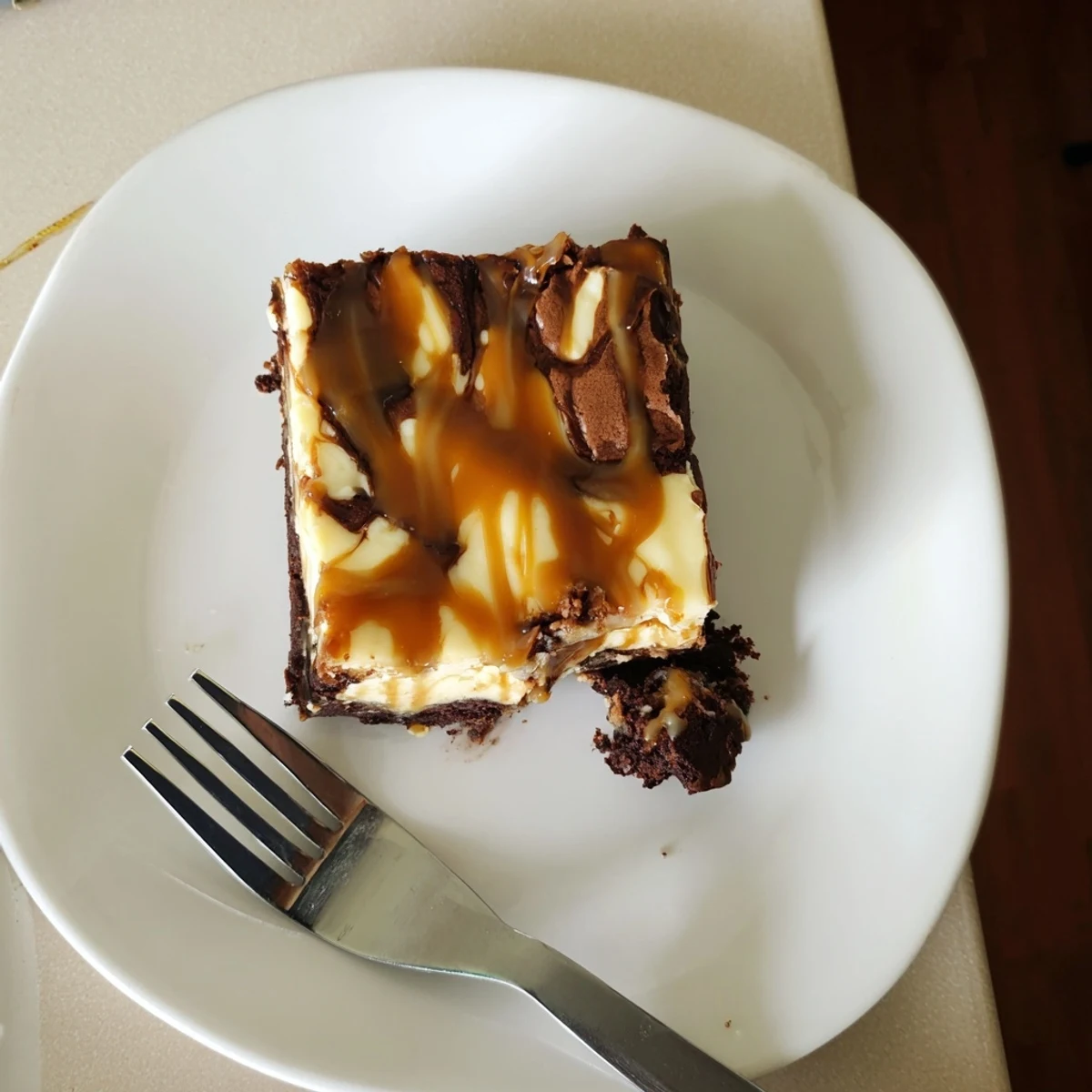 Slice of caramel brownie cheesecake bliss featuring three indulgent layers of chocolate brownie, smooth cheesecake, and glossy caramel glaze finished with optional pecans