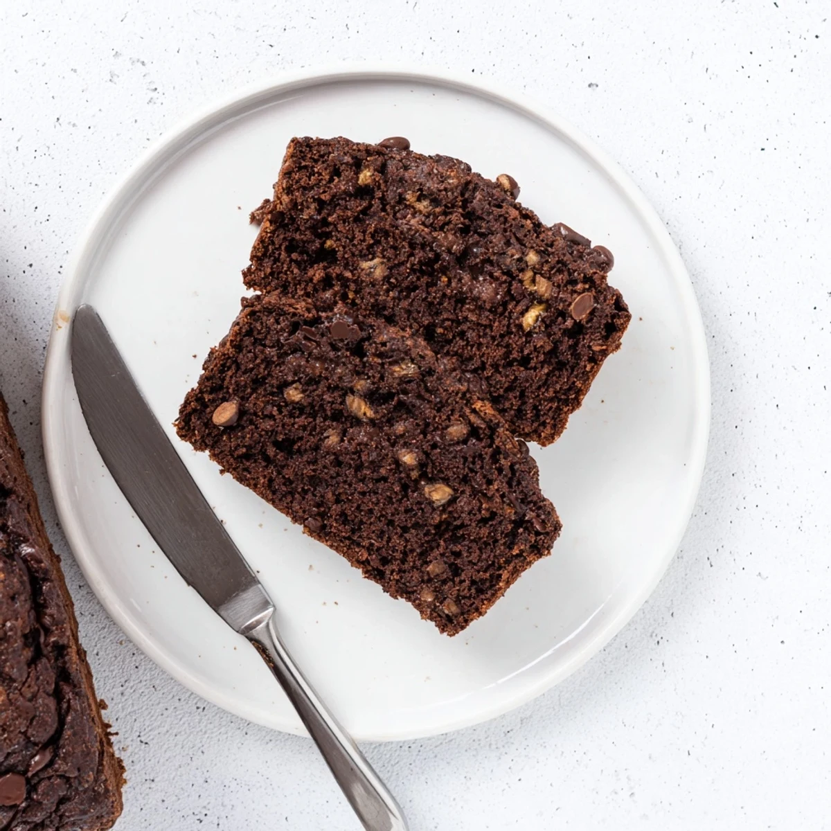 Slice of rich chocolate espresso banana bread served warm on a white plate with butter melting
