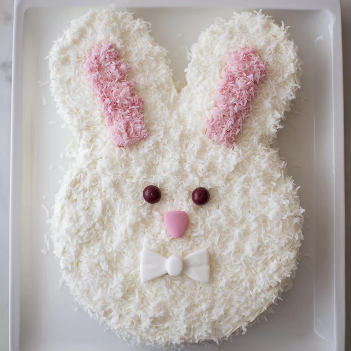 Whimsical bunny-shaped cake decorated with coconut fur, fondant ears, and jelly bean face details