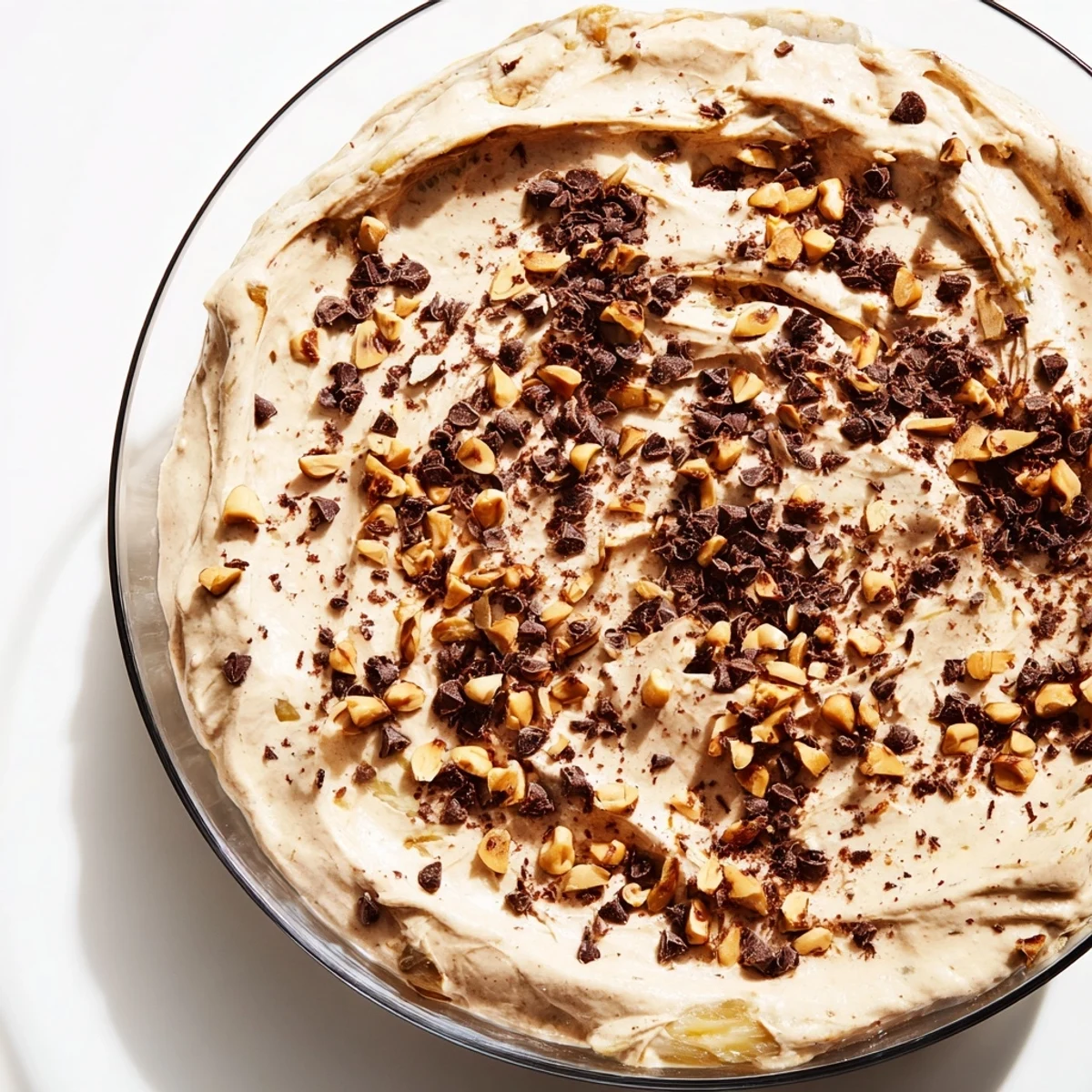 Creamy peanut butter and Cool Whip mousse topped with chopped roasted peanuts and mini chocolate chips in a clear glass bowl