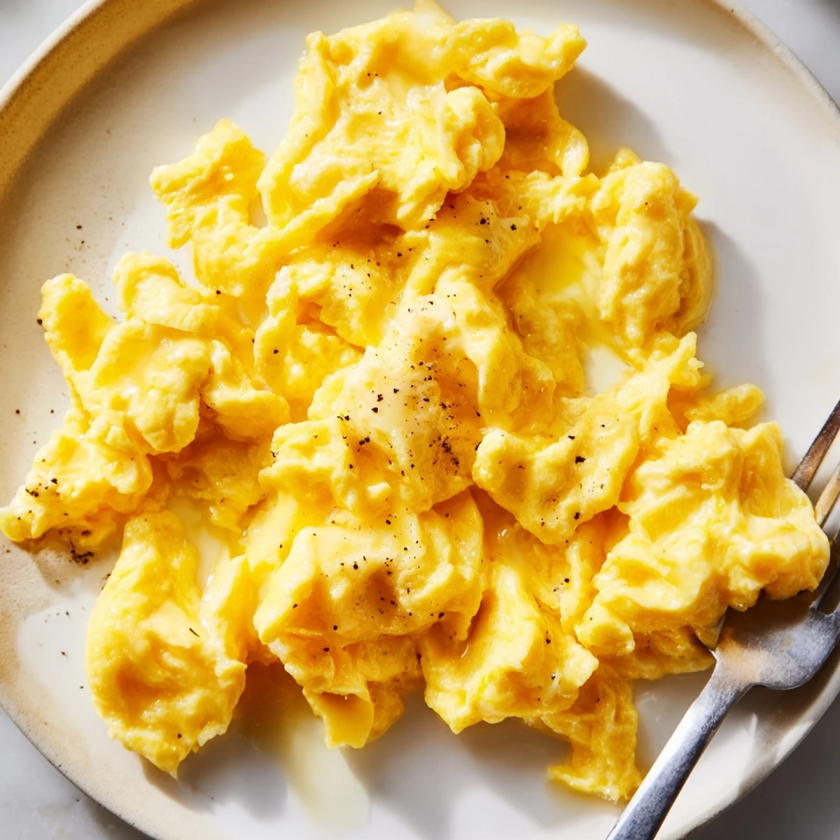 Fluffy scrambled eggs garnished with black pepper beside sliced avocado and toast