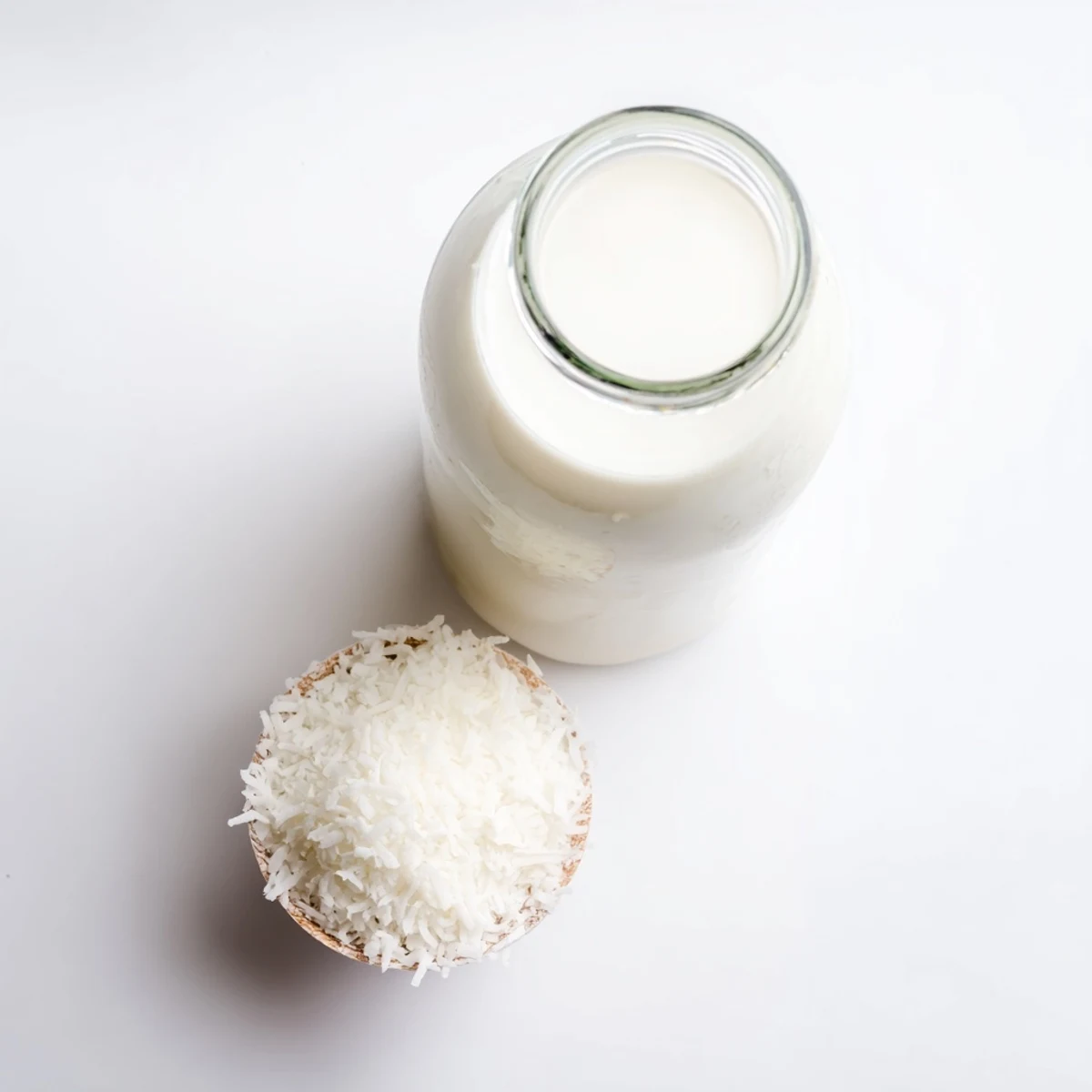 Glass of coconut milk poured next to shredded coconut and blender