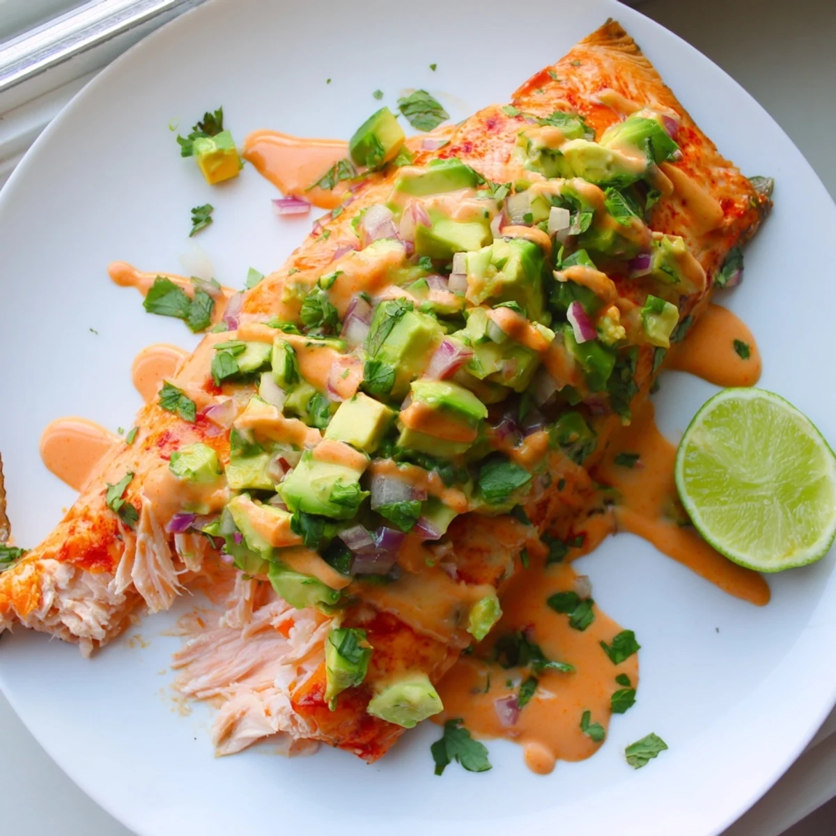 Crispy edged bang bang salmon topped with vibrant green avocado cucumber salsa on a white plate